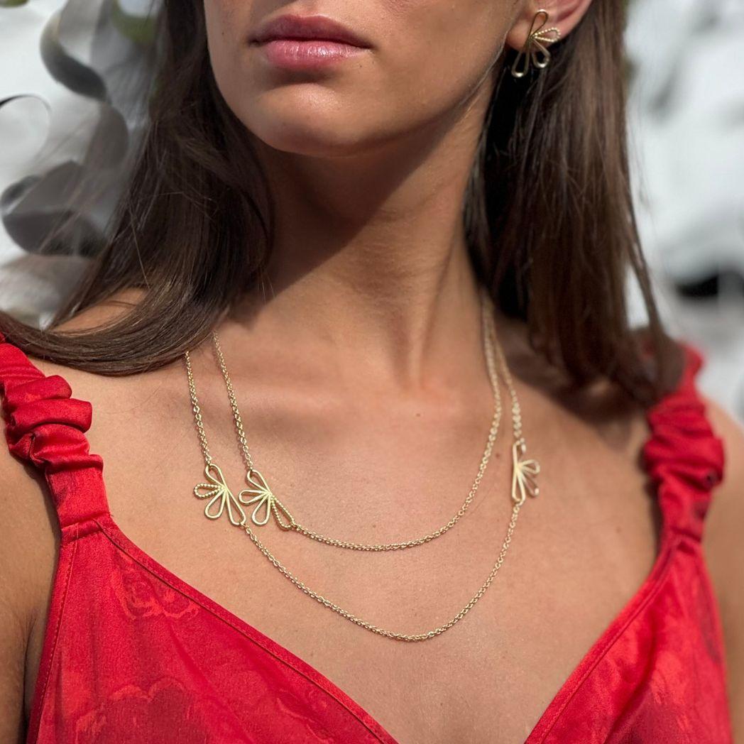 Guldhalsband med blomform på modell med röd sommarklänning 